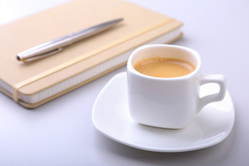 stylish notebook, ballpoint pen and white cup with a fragrant espresso coffee on the office desk.