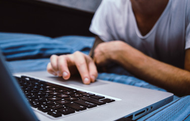 Close up of man's hands using computer, surfing on internet and relaxing on bed