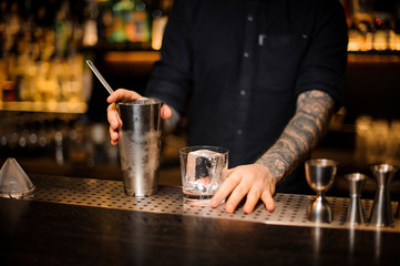 Fototapeta na wymiar Bartender holding a glass with ice cube and steel shaker