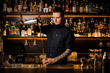 Professional bartender pouring the cocktail from the steel shaker