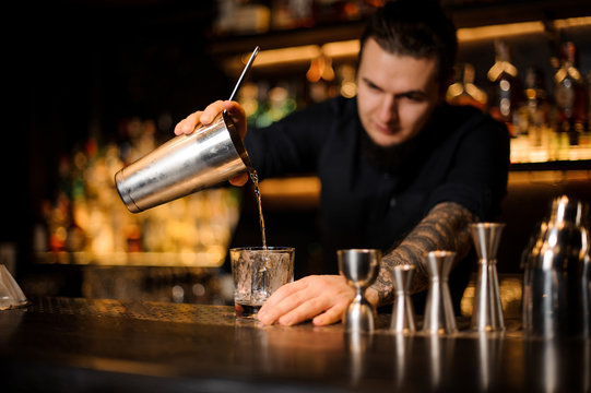 Professional bartender pouring a cocktail from the steel shaker