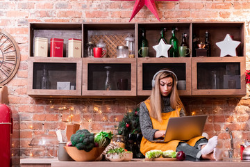 Serious young girl freelancer with blond hair working at a Loft kitchen with laptop in gray...