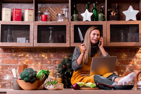 Blonde girl freelancer sitting at home in the loft kitchen with a laptop, talking on the phone and crying. Concept girl blonde who forgot about. holiday atmosphere
