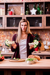 Girl with a displeased face is looking at broccoli in a bright loft kitchen. The girl does not like broccoli. Wooden plate with vegetables on a light wooden table.