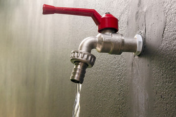 Red faucet isolate on grey background with flowing water