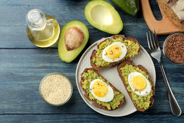 Sandwich with avocado puree and egg on a plate and ingredients for cooking on a blue wooden table. view from above
