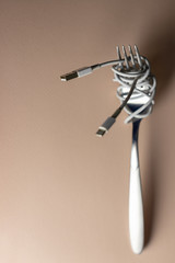 beige background. charging cord, dressed in a dining fork. spaghetti