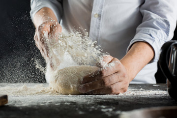 Cook sprinkles dough with flour on the kitchen table