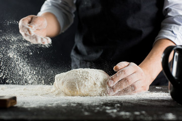 A chef in a black apron sprinkles flour on the kitchen table with flour