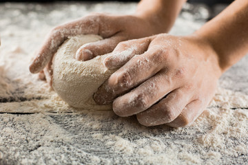 Male chef hands knead dough with flour on kitchen table