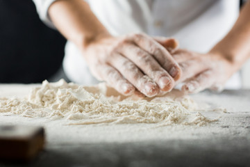 Male chef hands knead the dough with flour on the kitchen table