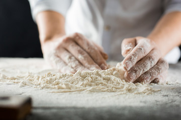 Male chef hands knead the dough with flour on the kitchen table