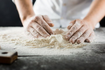 Obraz na płótnie Canvas Male chef hands knead the dough with flour on the kitchen table