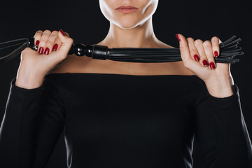 partial view of strict woman holding leather flogging whip isolated on black
