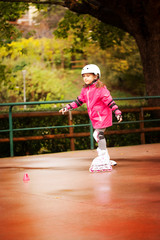 Fototapeta premium A little caucasian girl beginner roller in the autumn park in the rainy day.