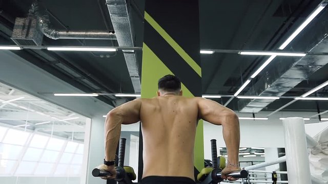 Powerful boy doing pull-ups on the parallel bars during his training.
