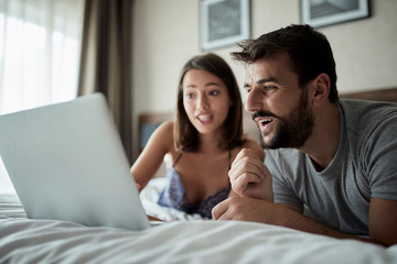 people, family, bedtime and fun concept -Man and woman watching video on laptop and laughing together.