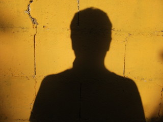 PRESENCIA - Sombra de una persona sobre una pared amarilla - obrazy, fototapety, plakaty