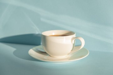 Cup of steaming coffee on seafoam green background in natural sunlight. Abstract photo of hot espresso drink on pale blue-green table