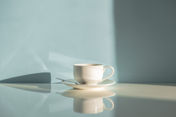 Cup of steaming coffee on seafoam green background in natural sunlight. Abstract photo of hot espresso drink on pale blue-green table and wall