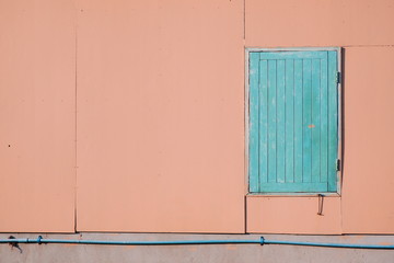 The old wooden blue window in pink fiber cement board wall with water pipeline on concrete wall in urban home exterior  concept