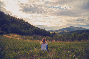Girl sitting on a green meadow and watching the countryside landscape. - Powered by Adobe