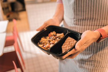 Waiter holding lunch box with stewed vegetables and meat steak