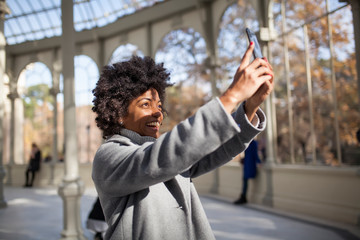 Afro woman having fun with her smart phone in the park, take a picture