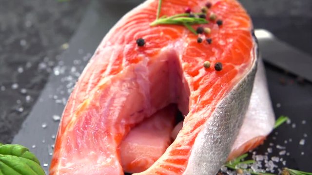 Salmon. Raw trout fish steak with herbs and lemon on black slate background. Cooking, seafood. Healthy eating concept, dieting. Slow motion 4K UHD video footage. 3840X2160
