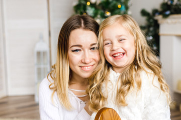 Merry Christmas and happy holidays Parent and little child, with pleasure near the Christmas tree indoors. Loving family with gifts in the room.