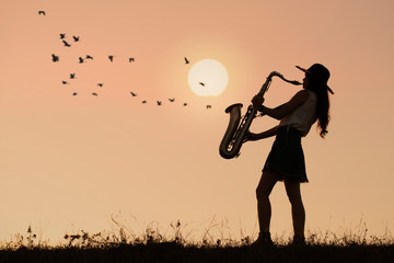Woman play saxophone with sunset or sunrise background