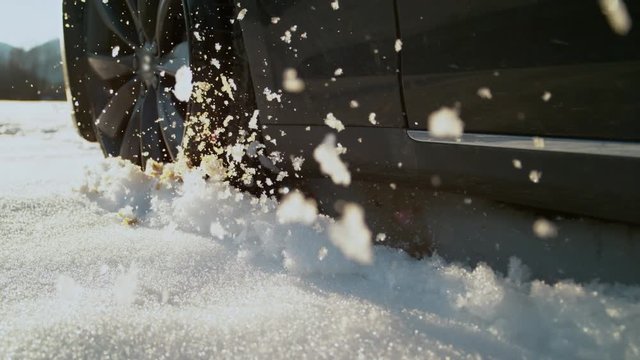 SLOW MOTION SPEED UP, CLOSE UP, LENS FLARE Car driving off road on sunny day spitting up pieces of snow. Driver enjoying slippery winter conditions in his powerful car. Winter tyre losing traction