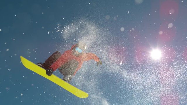 SLOW MOTION WARP, LENS FLARE, CLOSE UP Young pro snowboarder jumps off kicker and does a spinning trick. Spectacular shot of winter athlete riding his snowboard and doing a grab high in the sunny sky