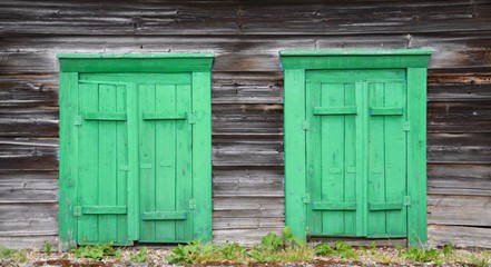 Fototapeta na wymiar Two small green village windows in an old gray wooden wall. Leaving for landrams in an abandoned house