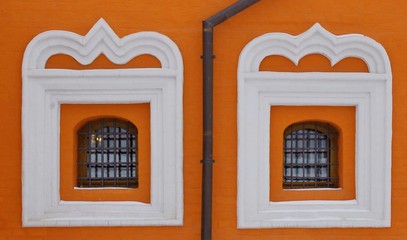 Two small church windows with wooden frames and white edging in an orange stone wall, divided by a sewer
