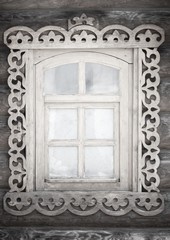 A small antique rustic window with carvings in a wooden wall in black and white format.