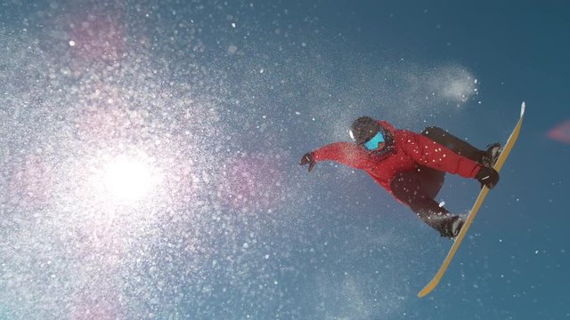 SLOW MOTION SPEED UP, CLOSE UP, LENS FLARE Bright sun shines on pro snowboarder jumping kicker and doing a trick in the picturesque winter sky resort. Awesome shot of rider grabbing his board mid-air