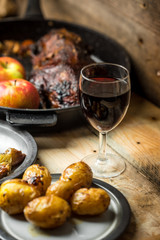 goose baked with apples and potatoes, next to a glass of red wine on a wooden background, rustic table