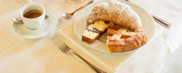 Breakfast. Coffee, cutlery and plate with a croissant, a sponge cake and a slice of cake