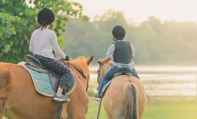 Kids learn to ride a horse near the river before sunset.