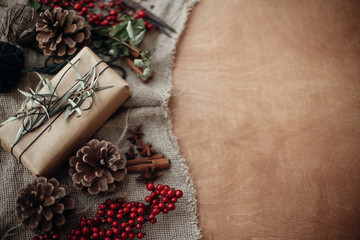 Stylish rustic christmas gift box with green branch and fir branches, berries, anise, pine cones, cinnamon on rustic wooden background. Simple eco present. Atmospheric mood. Space for text