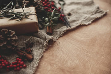 Stylish rustic christmas gift box with green branch and fir branches, red berries, pine cones,...