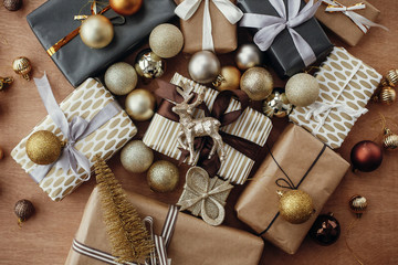 Merry Christmas. Christmas stylish gift boxes with glitter reindeer and ornaments on rustic wooden background. Modern black and gold presents flat lay. Seasons greetings.
