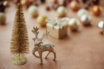 Christmas golden glitter tree and reindeer on background of gift box, shiny baubles and balls on rustic background. Modern gold decorations and present. Seasons greetings. Merry Christmas