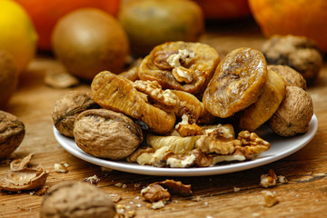 Dried fig and whole and cracked walnuts on white ceramic plate. Wooden table and various citrus in the background.