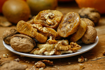 Dried fig and whole and cracked walnuts on white ceramic plate. Wooden table and various citrus in the background.