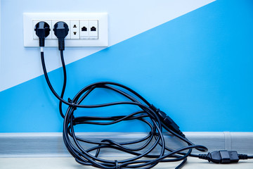 a white plastic multiple outlet mounted on a light wall with copy space for text, plugs with a twisted pile of black cable are included in the socket.