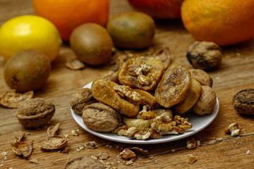 Dried fig and whole and cracked walnuts on white ceramic plate. Wooden table and various citrus in the background.