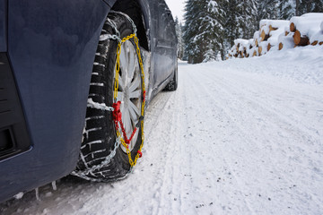 Snow chains mounted on front car tire in winter conditions with snow track and ice.