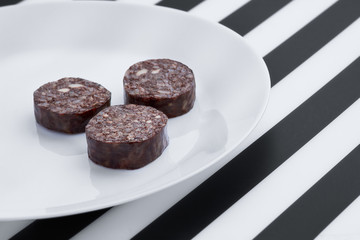 Black pudding on black and white striped background. Morcilla de Burgos